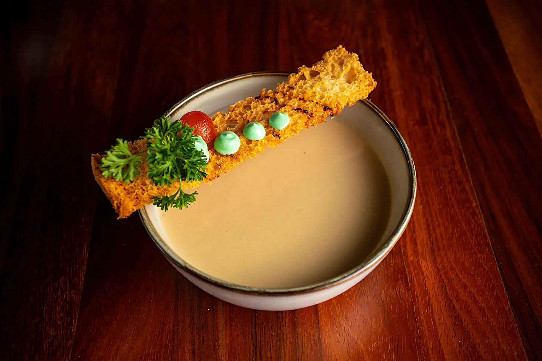 Crema de champiñón en un plato hondo, con un pan crocante, tomatillo y una hoja de especialidad Cena Show de hotel Oceano Palace Mazatlán