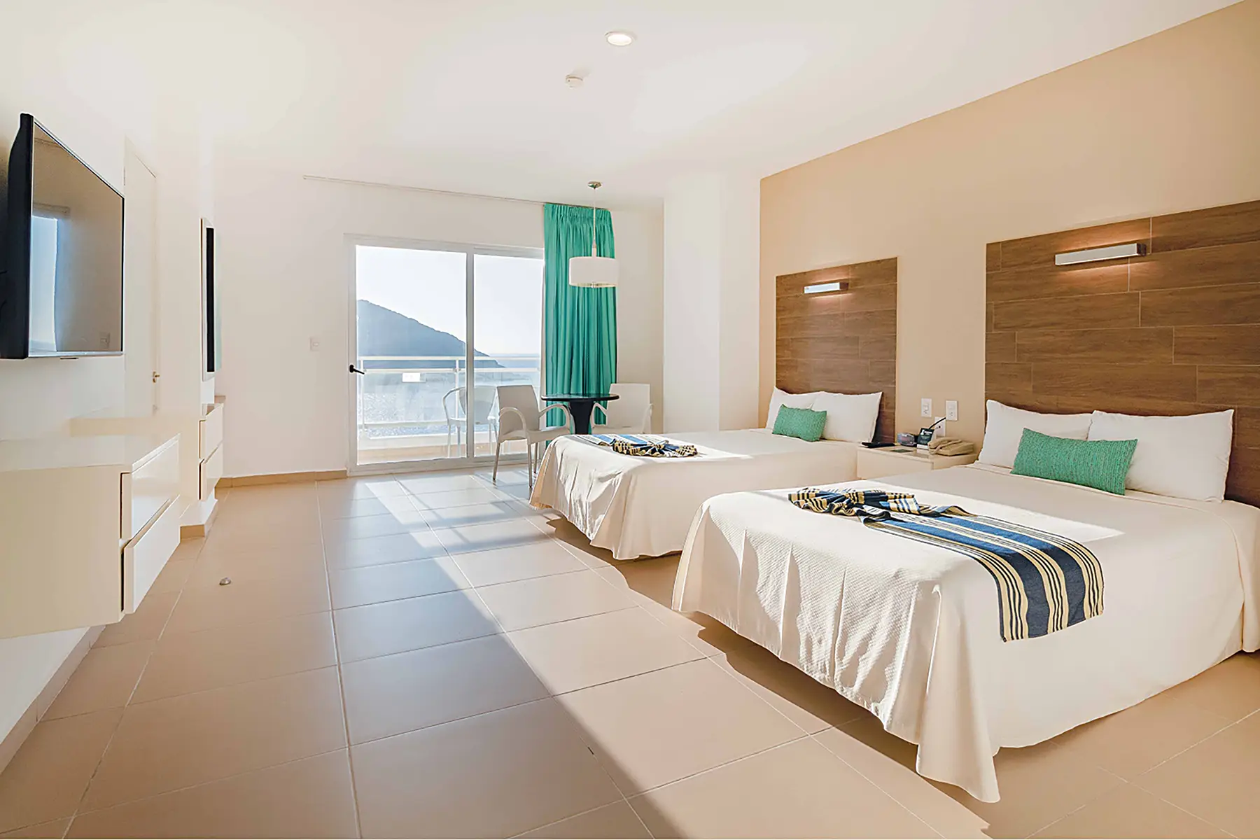 Habitación junior suite vista al mar, en Zona Dorada Mazatlán, dos camas, tv, mesa con dos sillas, mobiliario,luminaria, hotel pacific palace